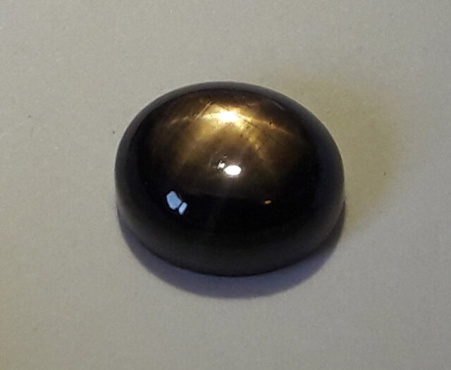 Polished black star sapphire gemstone displaying a pale asterism star