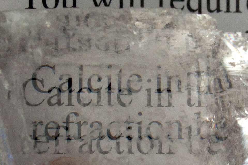 Transparent Iceland spar calcite crystal showing double refraction of printed text